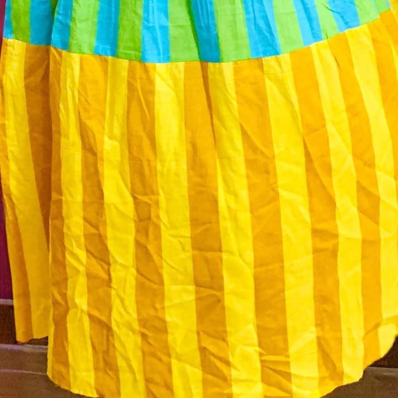 Puede incluir: Una tela colorida con rayas verticales amarillas y naranjas, que transicionan a bandas verdes y azules en la parte superior. La tela parece ligera, posiblemente utilizada para ropa o decoraci&oacute;n del hogar.