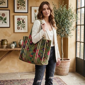 May include: A large, rectangular, quilted tote bag in olive green velvet featuring a vibrant floral and bird pattern in shades of pink, purple, and red. The bag has two sturdy shoulder straps with a cream-colored braided trim along the edges.