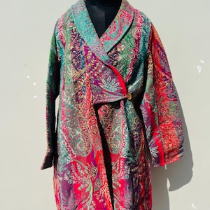 May include: A long, colorful coat with a paisley pattern in shades of red, purple, green, and teal. The coat has long sleeves, a shawl collar, and a single button closure. The garment is displayed on a black mannequin.