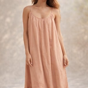 May include: A peach-colored maxi dress with thin spaghetti straps and a scoop neckline. The dress has a gathered bodice and a ruffled hemline. The fabric appears to be lightweight and flowing, suitable for warm weather. The dress is a solid color and has a simple, elegant design.