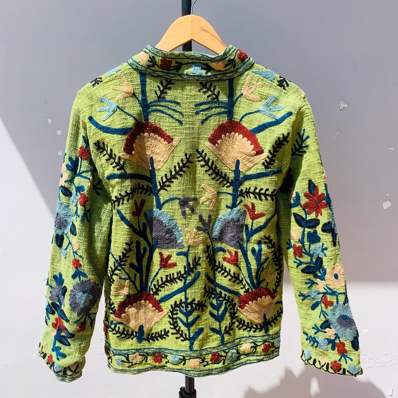 May include: A lime green jacket with long sleeves and a collared neckline. The jacket is adorned with colorful floral embroidery in shades of red, blue, tan, and black. The embroidery covers the front, back, and sleeves of the jacket.