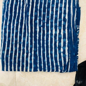 May include: Folded indigo blue fabric with a white vertical stripe and blue dot pattern. The fabric appears to be cotton or a similar natural fiber. The design is reminiscent of traditional block printing.