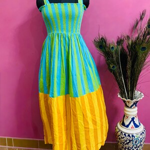 Puede incluir: Un vestido largo a rayas de colores vibrantes, azul, verde y amarillo. El vestido presenta un corpi&ntilde;o ajustado y una falda fluida. El vestido se exhibe en un maniqu&iacute;.