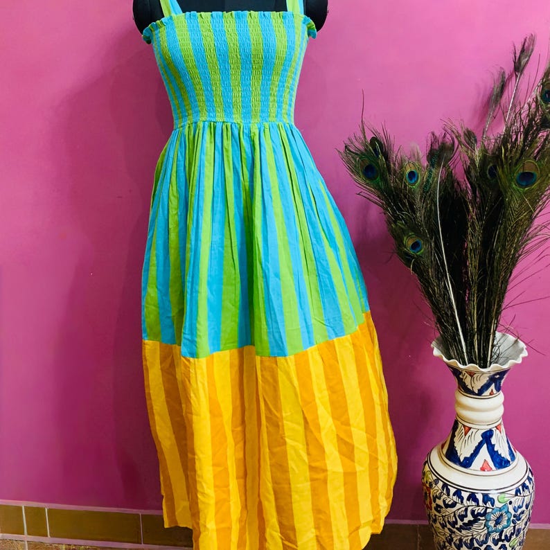 Puede incluir: Un vestido largo a rayas de colores vibrantes, azul, verde y amarillo. El vestido presenta un corpi&ntilde;o ajustado y una falda fluida. El vestido se exhibe en un maniqu&iacute;.