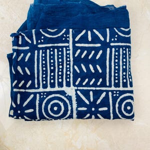 May include: A folded indigo blue fabric with a white geometric pattern. The design features squares, circles, and lines. The fabric is layered with a solid indigo blue textile.