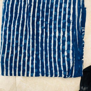 May include: Folded fabric with a blue and white pattern. The design features vertical white stripes and scattered blue polka dots against a dark blue background. The fabric appears to be cotton or a similar material.