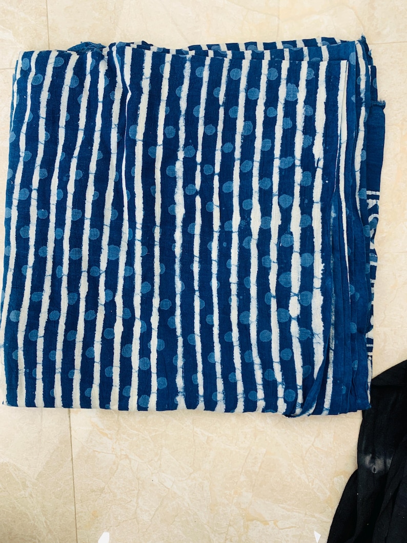 May include: Folded fabric with a blue and white pattern. The design features vertical white stripes and scattered blue polka dots against a dark blue background. The fabric appears to be cotton or a similar material.
