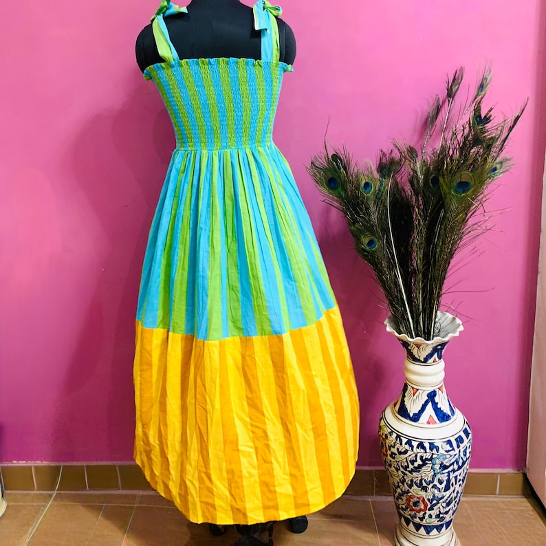Puede incluir: Un vestido de verano a rayas de colores en un maniqu&iacute;. El vestido presenta un corpi&ntilde;o a rayas azules y verdes, una falda a rayas azules y verdes y un dobladillo a rayas amarillas. El vestido tiene tirantes verdes.