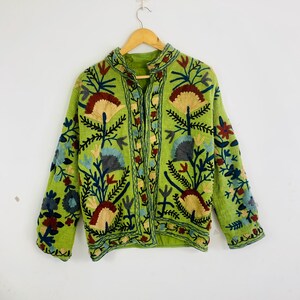 May include: A light green jacket with intricate floral embroidery in shades of red, blue, and yellow. The jacket features a mandarin collar and long sleeves, with a button-up front. The embroidery creates a textured, decorative effect.