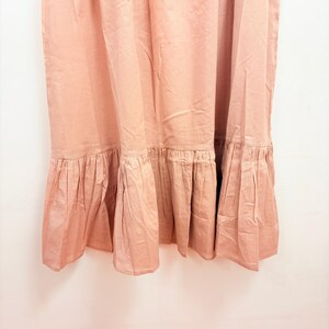 May include: A dusty rose-colored dress with a ruffled hem. The fabric appears to be a lightweight material, with vertical folds and subtle variations in tone. The ruffled hem adds a decorative element to the bottom of the dress.