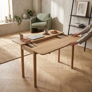 Op de afbeelding: Een bureau van lichtgekleurd hout met een rechthoekig blad dat opengeschoven kan worden om een verborgen opbergvak te onthullen. Het bureau heeft vier cilindervormige poten en een gladde afwerking voor een functionele werkplek met geïntegreerde opbergruimte.