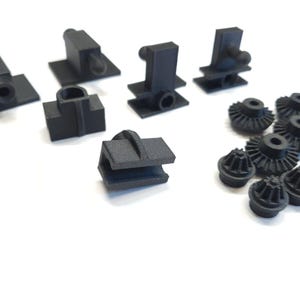Peut inclure: Diverses pièces noires imprimées en 3D, comprenant des formes variées avec des bases rectangulaires, des éléments cylindriques et des structures en forme d'engrenage. Les pièces sont disposées sur une surface blanche, mettant en valeur leurs conceptions.