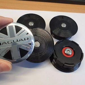 Puede incluir: Cuatro tapacubos circulares con acabado cromado, un diseño de bandera Union Jack negra y la palabra JAGUAR grabada en el centro. Las tapas tienen bases de plástico negro texturizado impresas en 3D con una fijación central de perno metálico.