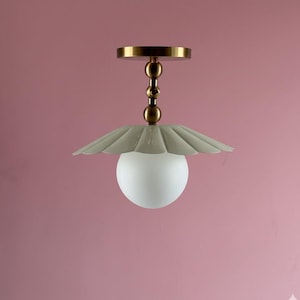 May include: A modern ceiling light fixture with a brass finish. The light has a scalloped, pale green shade and a frosted globe. The fixture is suspended from a brass canopy and has a decorative brass rod.