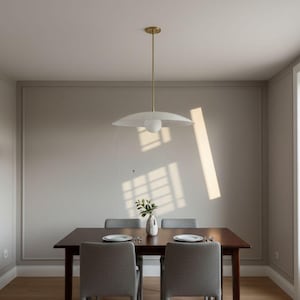 May include: A dining room scene featuring a dark wood table with four gray upholstered chairs. A white, saucer-shaped pendant light hangs above. A small vase with greenery sits on the table, with two plates. The room has light-colored walls and hardwood floors.