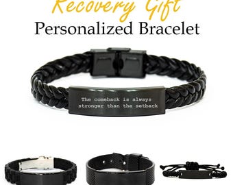 May include: Black braided leather bracelet with a rectangular metal plate engraved with the text "The comeback is always stronger than the setback." The image also shows three other black bracelets with different designs. The text "Recovery Gift Personalized Bracelet" is at the top.