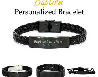 Könnte beinhalten: Schwarze personalisierte Taufarmbänder. Das Hauptarmband hat ein geflochtenes Lederband mit Metallverschluss und eine rechteckige Platte mit der Gravur "Getauft in Christus" und dem Datum. Zusätzliche Armbandstile werden gezeigt.