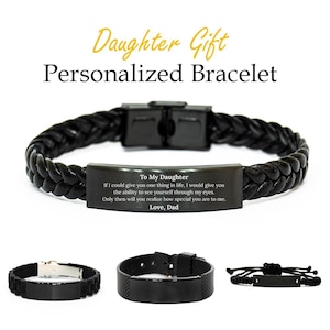Puede incluir: Pulsera de cuero negro trenzado con una placa metálica rectangular grabada con un mensaje. El texto dice "To My Daughter" seguido de un mensaje de "Love, Dad". Se muestran pulseras negras adicionales.