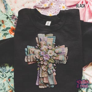 May include: Black crewneck sweatshirt featuring a detailed cross design. The cross is adorned with floral and patchwork quilt elements in pastel colors. The text "Cotton & Chaos" is visible in the lower right corner.
