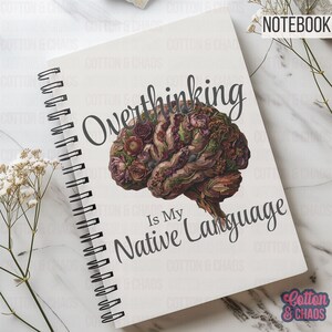 May include: White spiral-bound notebook with the text "Overthinking Is My Native Language." The cover features a detailed illustration of a brain composed of flowers in shades of brown, purple, and green. The word "NOTEBOOK" is in the top right corner.