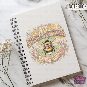 May include: A spiral-bound notebook with a bee-themed design. The cover features a detailed illustration of a bee with a pink bow, surrounded by floral elements and the text "SWEET AS HONEY, STUNG A FEW TIMES". The word "NOTEBOOK" is at the top.