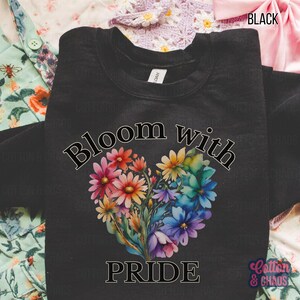 May include: Black crewneck sweatshirt with the words "Bloom with Pride" and a heart-shaped floral design in vibrant colors. The sweatshirt has a tag that says "LDAN" and the brand name "Cotton & Chaos" is in the bottom right corner.