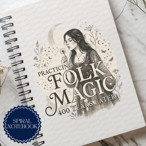 May include: A spiral notebook featuring a cover illustration of a person holding a dandelion, surrounded by botanical elements, a crescent moon, and butterflies. The text reads "PRACTICING FOLK MAGIC 400 YEARS LATER" in a decorative serif font.