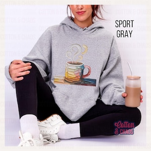 May include: Sport gray hoodie with a colorful coffee cup graphic. The cup features a rainbow design and steam rising from the top. The text "Cotton & Chaos" is visible in the lower right corner. The hoodie is a comfortable, casual style.