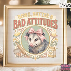 May include: A framed canvas print with a vintage-style illustration. The artwork features an opossum wearing a pink bow, surrounded by baking-related elements like butter, eggs, and flour, with the text "BOWS, BUTTER & BAD ATTITUDES". The print is in a gold frame.