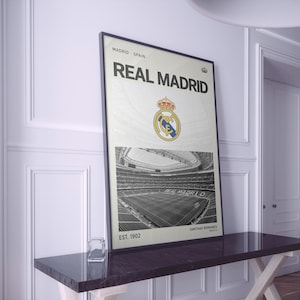 Puede incluir: Un póster enmarcado que presenta el logotipo del Real Madrid y una fotografía en blanco y negro del estadio Santiago Bernabéu. El texto dice Madrid Spain, Real Madrid, Est. 1902 y Santiago Bernabéu. El diseño incluye un pequeño icono de corona.