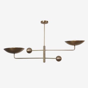 Puede incluir: Una lámpara de araña moderna de latón con un diseño minimalista. Cuenta con una barra vertical central con brazos horizontales que sostienen pantallas en forma de cuenco. El accesorio tiene un acabado metálico cálido y está suspendido del techo.