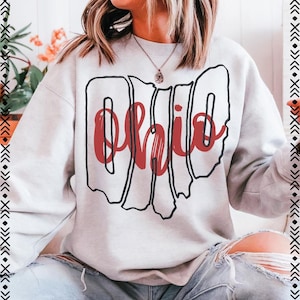 May include: A light gray sweatshirt with the word "Ohio" in red script, outlined in black. The word is stylized to resemble the shape of the state. The sweatshirt is a casual style.