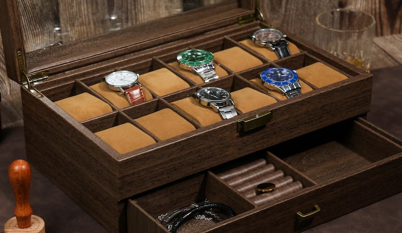 May include: A wooden watch box with a clear lid, showcasing several wristwatches with various colored faces and bands. The box has multiple compartments with tan cushions, and a lower drawer for additional storage.