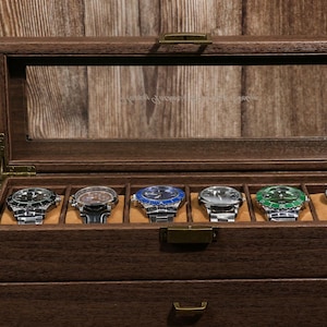 May include: A wooden watch display case with a glass top, showcasing six wristwatches with various colored faces and metal bands. The case is made of dark wood and has a drawer.