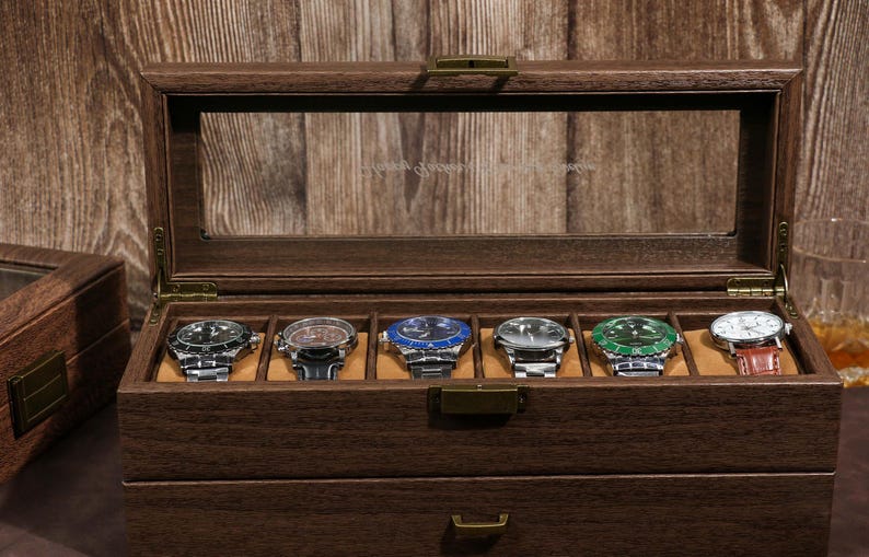 May include: A wooden watch display case with a glass top, showcasing six wristwatches with various colored faces and metal bands. The case is made of dark wood and has a drawer.
