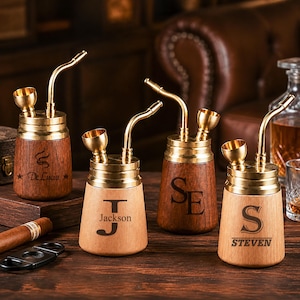 May include: Four wooden smoking pipes with brass tops, curved stems, and bowls. Each pipe features unique laser-engraved text: De Lucia, J Jackson, SE, and S STEVEN. The pipes are arranged on a dark wooden surface alongside a cigar and cutter.
