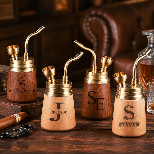 May include: Four wooden smoking pipes with brass tops, curved stems, and bowls. Each pipe features unique laser-engraved text: De Lucia, J Jackson, SE, and S STEVEN. The pipes are arranged on a dark wooden surface alongside a cigar and cutter.