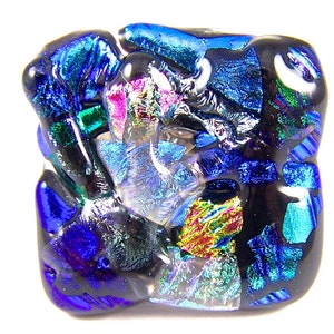 May include: A square-shaped piece of dichroic glass art with a blue, green, black, and iridescent color scheme.