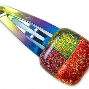 May include: A colorful hair clip with a rectangular, multi-colored glass design. The clip itself has a metallic finish with shades of blue, purple, and yellow. The glass design features red, green, and gold squares, adding a touch of sparkle.