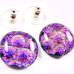 May include: A pair of purple and gold iridescent glass earrings with a black background. The earrings are round and have a textured surface.