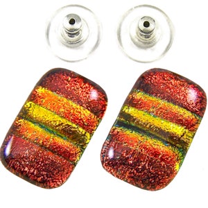 May include: A pair of rectangular dichroic glass stud earrings featuring horizontal stripes of vibrant red, orange, and yellow with a textured, metallic shimmer. Each earring includes a clear plastic and metal post back for secure attachment.