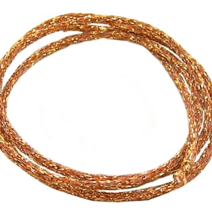 May include: Coiled copper-colored rope with a metallic sheen. The rope is tightly woven, creating a textured surface. The rope is arranged in a circular shape against a white background. The overall appearance suggests a decorative or craft item.