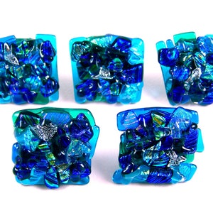 May include: Five square-shaped glass tiles with a mosaic design. The tiles are made of blue, green, and silver glass pieces.