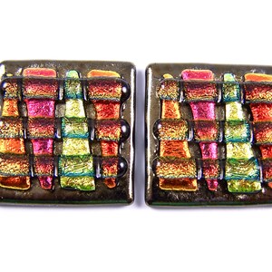 May include: A pair of square-shaped earrings with a geometric design. The earrings are made of glass and have a metallic finish. The glass is iridescent and features a rainbow of colors, including red, orange, yellow, green, blue, and purple.