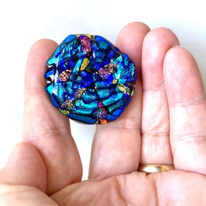 May include: A blue, green, and gold iridescent glass pendant with a textured surface.