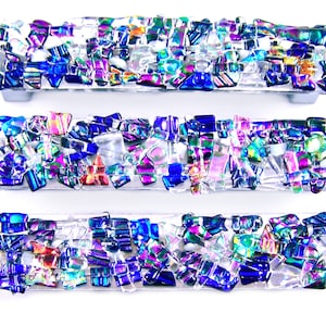 May include: Three iridescent glass cabinet pulls with a mosaic design. The pulls are made of small, irregular pieces of glass in shades of blue, purple, green, and white.