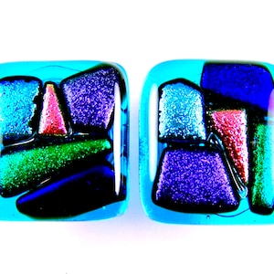 May include: A pair of square glass earrings with a mosaic design. The earrings are made of blue, green, purple, pink, and silver glass. The glass is textured and has a sparkly finish.