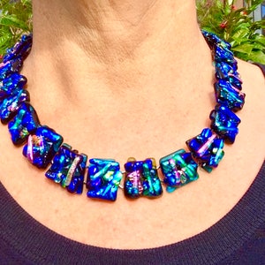 Peut inclure: Un collier en verre bleu avec des accents irisés. Le collier est composé de perles carrées de différentes couleurs et motifs.
