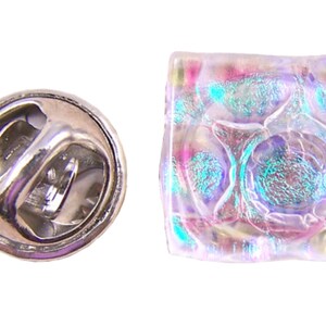 Peut inclure: Épingle carrée en verre irisé avec un fermoir argenté. Le verre présente un aspect texturé et bulleux avec des nuances de rose, de bleu et de violet. Le fermoir est de type papillon standard, en métal argenté brillant.