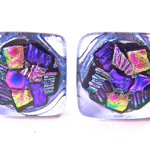 May include: A pair of square glass earrings with a black background and iridescent purple, pink, and gold accents.